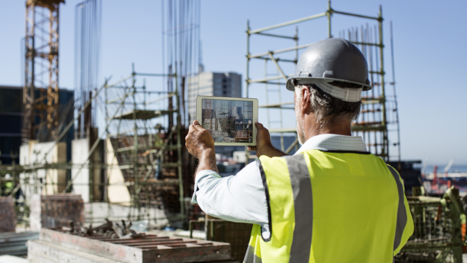 Rear view of male architect photographing construction site through digital tablet